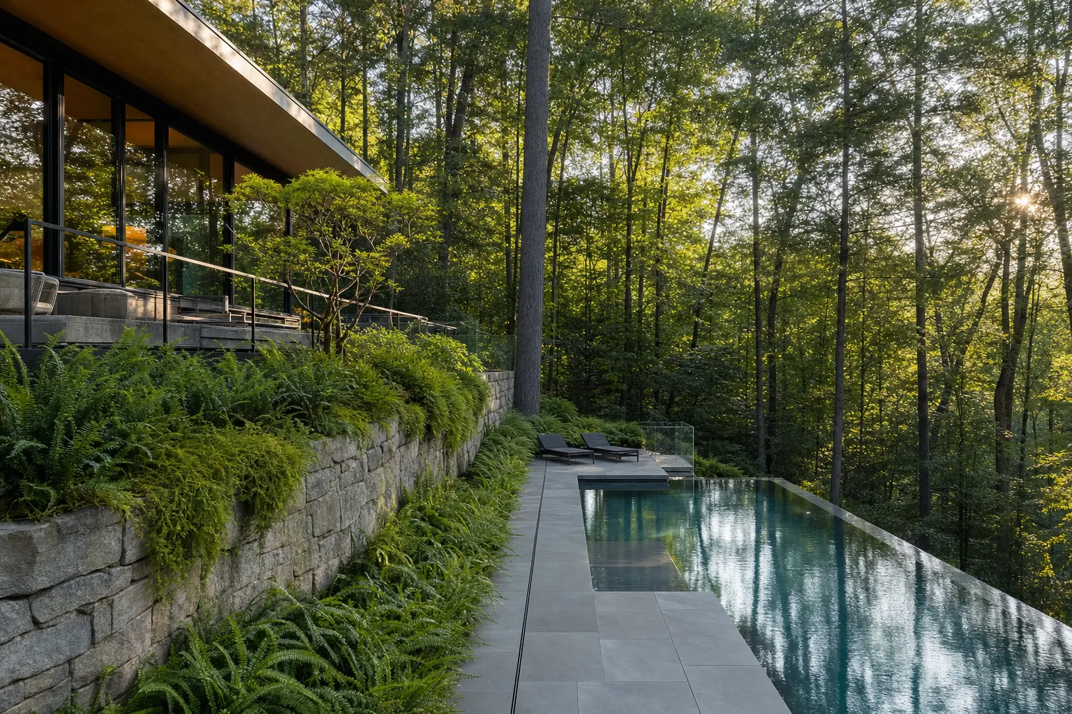 Modern pool on a wooded slope with a long stone retaining wall, ferns and a glass-walled home