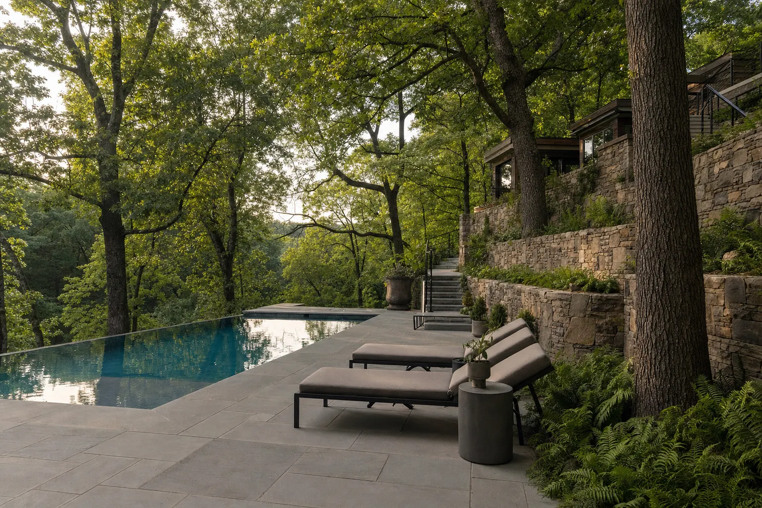 Pool terrace on a wooded slope with large old hardwoods kept around it, a stone retaining wall and ferns
